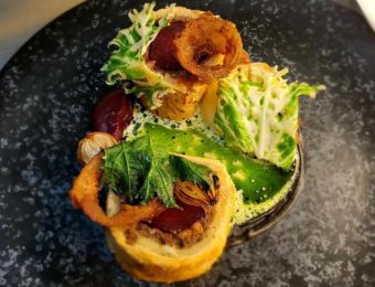 Gourmet dish with crispy onion rings, fresh leafy greens, and rich sauce on an elegant dark plate