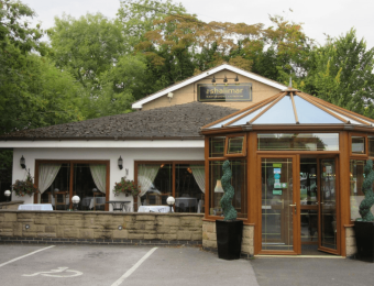 Entrance of a tandoori restaurant with glass conservatory and greenery in the background