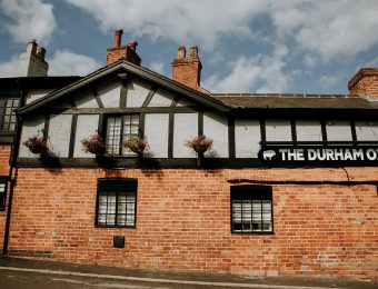 Historic brick pub with timber details named The Durham Ox under a blue sky with clouds