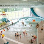 Indoor water park with families enjoying pools and slides, natural light streaming through large windows