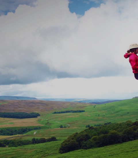 Person abseiling down a rock face in the Peak District with expansive green landscape views