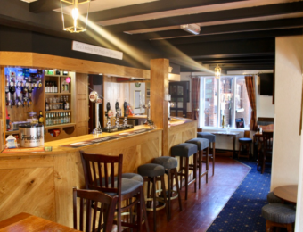 Cosy British pub interior with wooden bar, stools, and ambient lighting, inviting atmosphere for socialising
