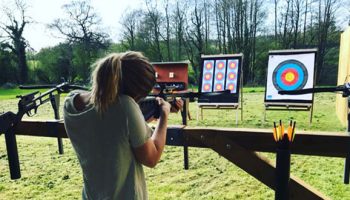 Person practising archery and shooting in an outdoor range with colourful target boards and wooded backdrop