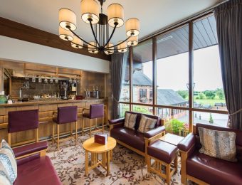 Cosy hotel bar lounge with leather seating, scenic countryside views through large windows, elegant chandelier overhead