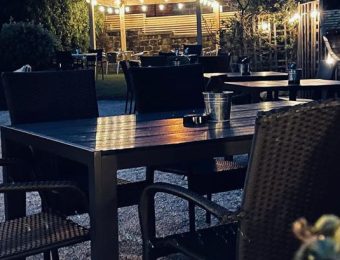Outdoor dining area with wicker chairs, wooden tables, and string lights creating a cosy evening ambiance