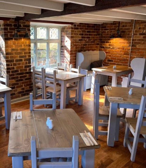 Cosy rustic café interior with wooden tables, chairs, and exposed brick walls, softly lit by natural sunlight
