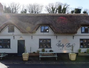 Thatched roof pub with outdoor benches, surrounded by trees, named The Holly Bush at Salt