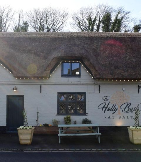 Thatched roof pub with outdoor benches, surrounded by trees, named The Holly Bush at Salt