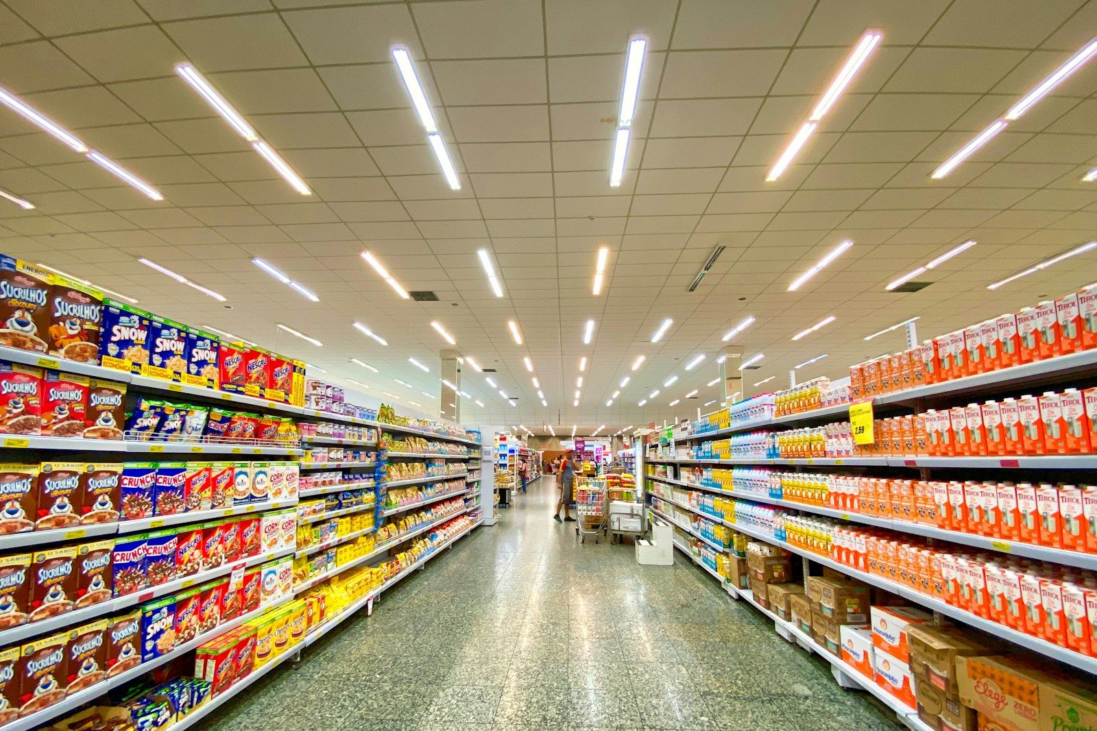 Wide supermarket aisle with bright lighting, showcasing shelves stocked with various cereals and packaged goods