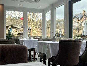 Elegant restaurant interior with large windows, overlooking a scenic view of a bridge and houses