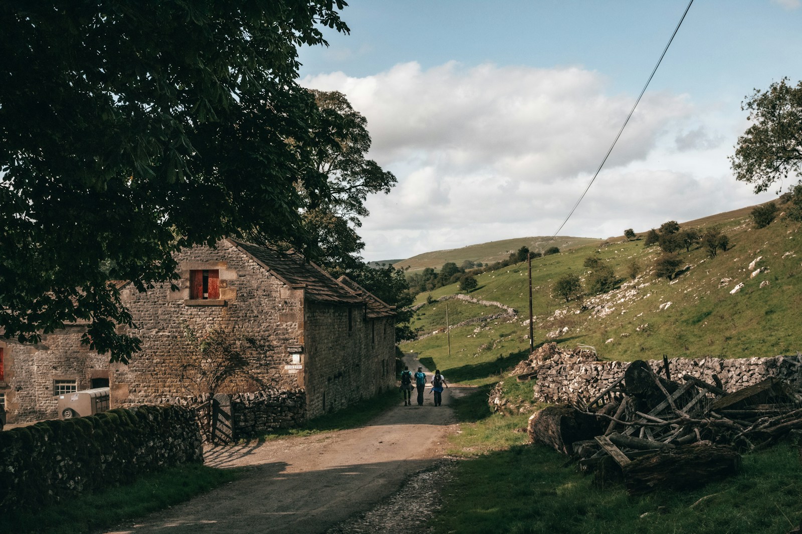 Rural stone cottage in lush green countryside with people walking down a scenic path under a clear blue sky