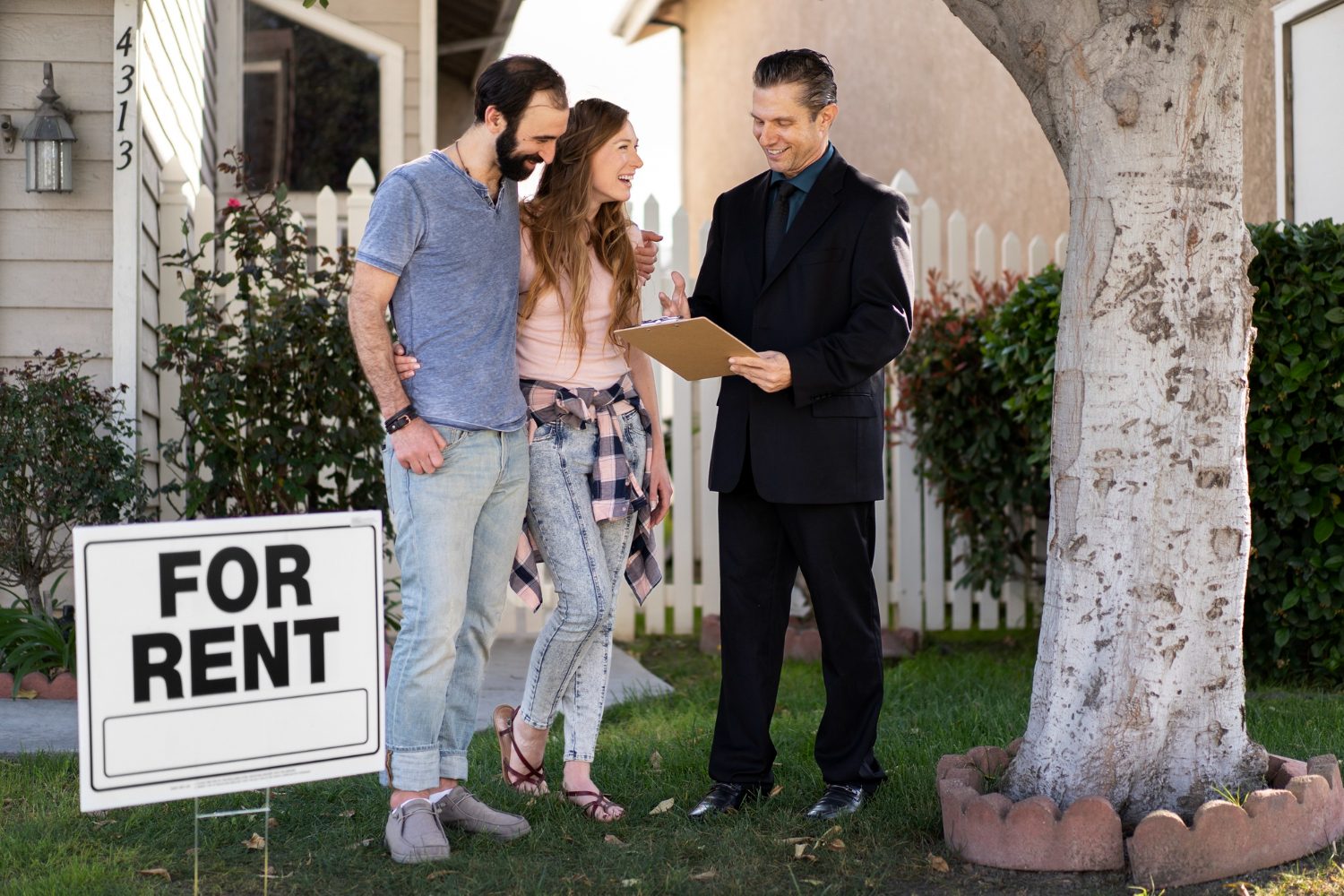 A couple stands in front of a "For Rent" sign, appearing hopeful as they consider their housing options