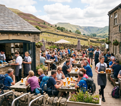People dining outdoors at a countryside pub, staff serving food and drinks, scenic hills in the background