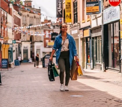 Woman walking down shopping street with bags in hand, enjoying a sunny day in the city